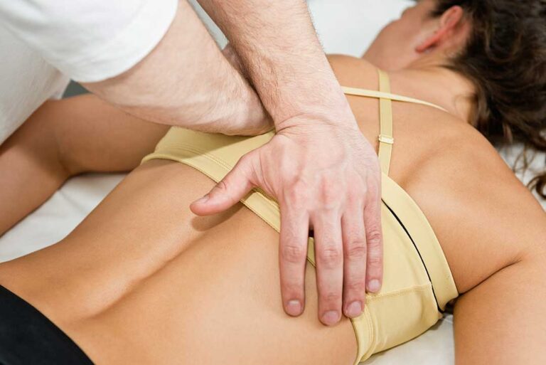 A chiropractor gently examines a middle-aged woman's back in a well-lit community health clinic.